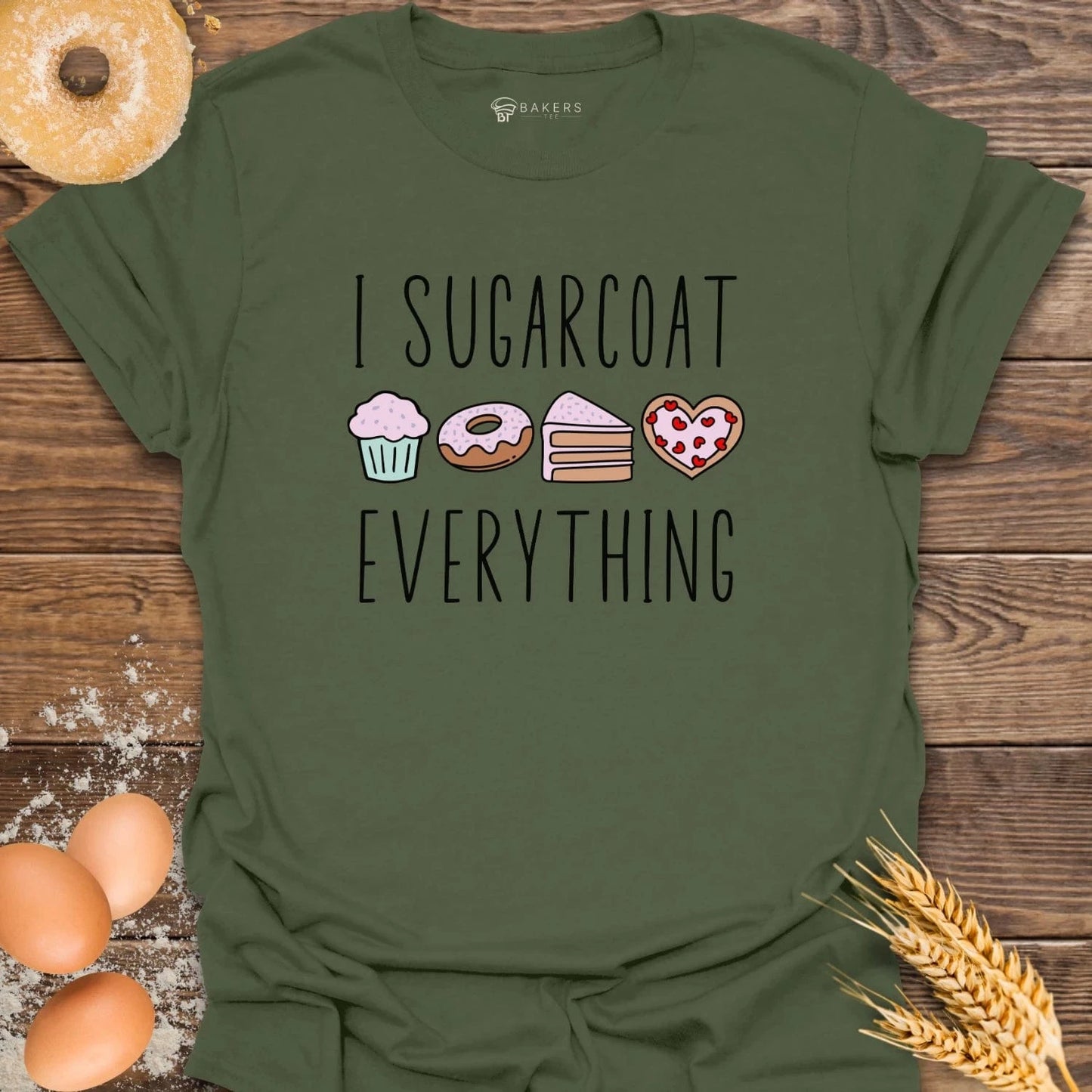 A Miltary crew neck T-shirt with the text 'I SUGARCOAT EVERYTHING' printed on the front, accompanied by graphic elements such as a muffin, a cupcake, a slice of pizza, and a cookie.