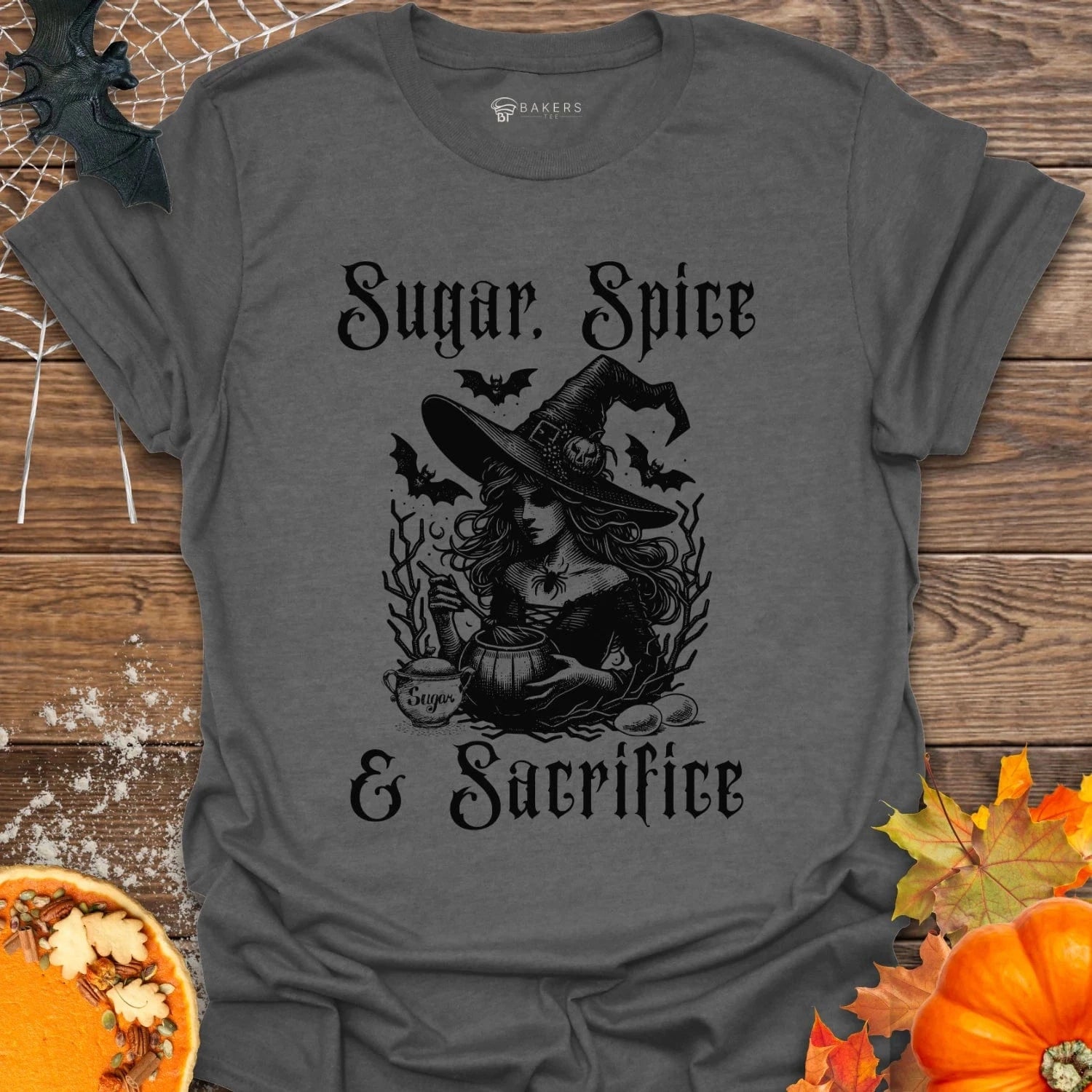 Gray t-shirt with Halloween-themed design featuring a witch and text on a wooden background with pumpkins and leaves.
