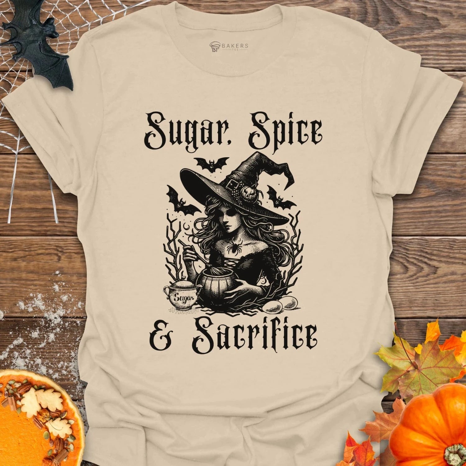 Beige t-shirt with Halloween-themed design featuring a witch and text on a wooden surface with pumpkins and leaves.