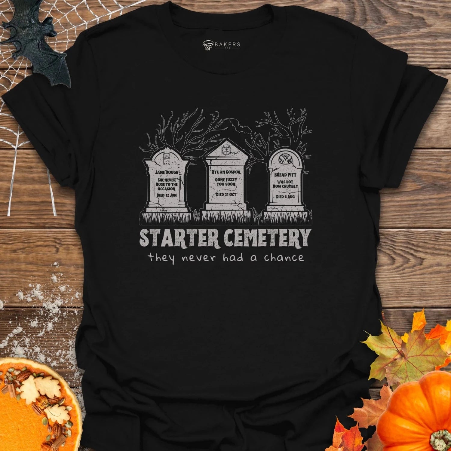 Black t-shirt with 'Starter Cemetery' design on a wooden surface with pumpkins and leaves.