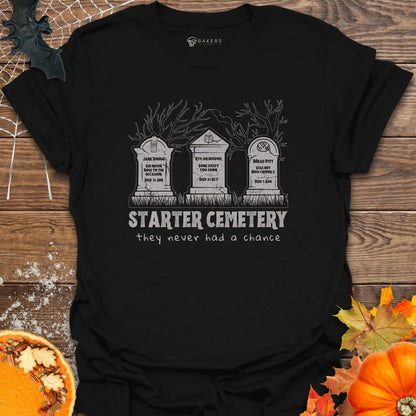 Black t-shirt with 'Starter Cemetery' design on a wooden surface with pumpkins and leaves.
