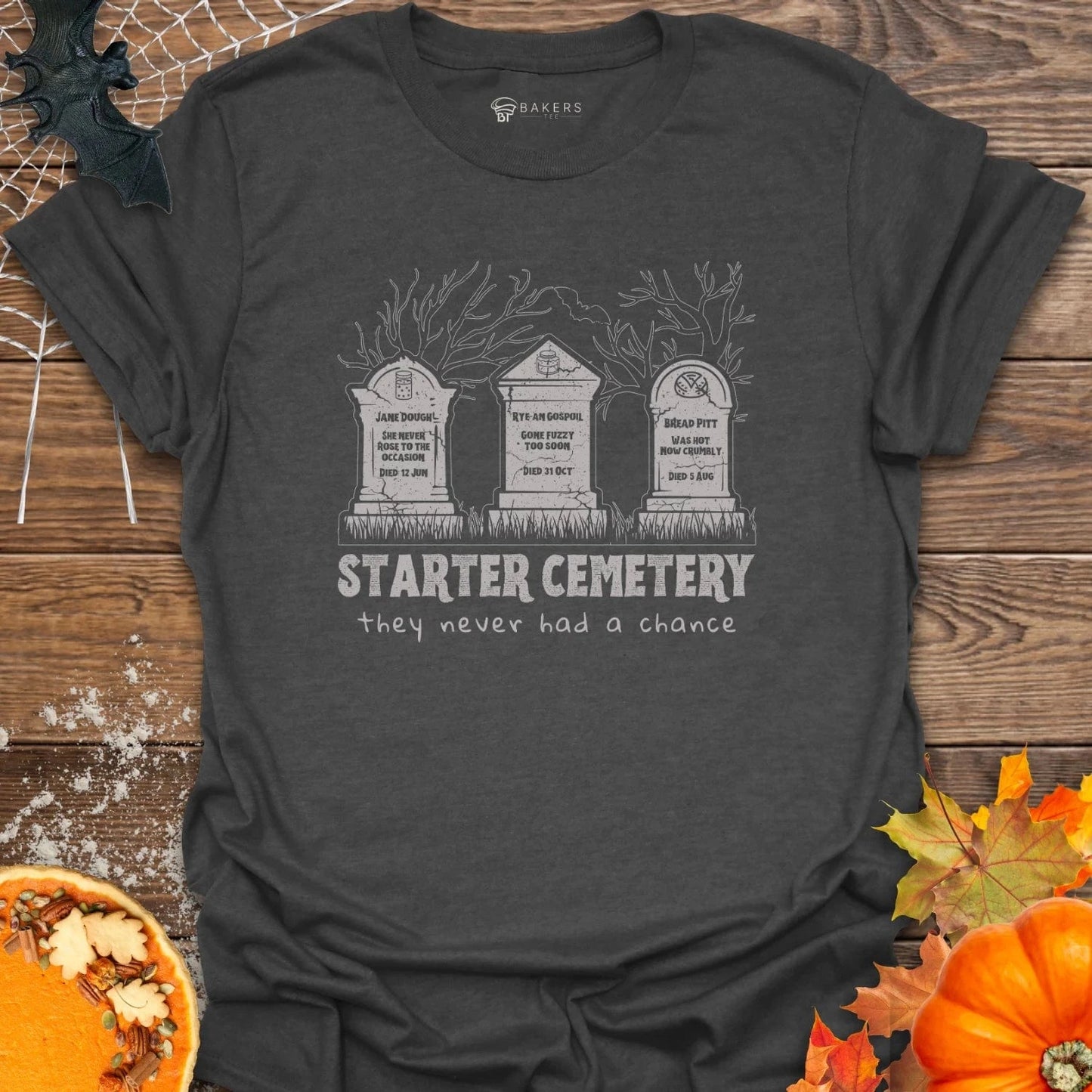 Dark gray t-shirt with 'Starter Cemetery' design on a wooden surface with pumpkins and leaves.