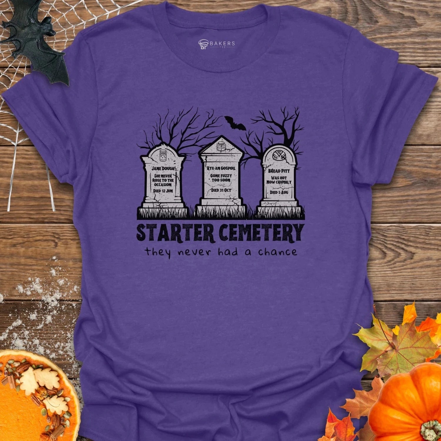Heather Purple t-shirt with 'Starter Cemetery' design on a wooden surface with Halloween decorations.