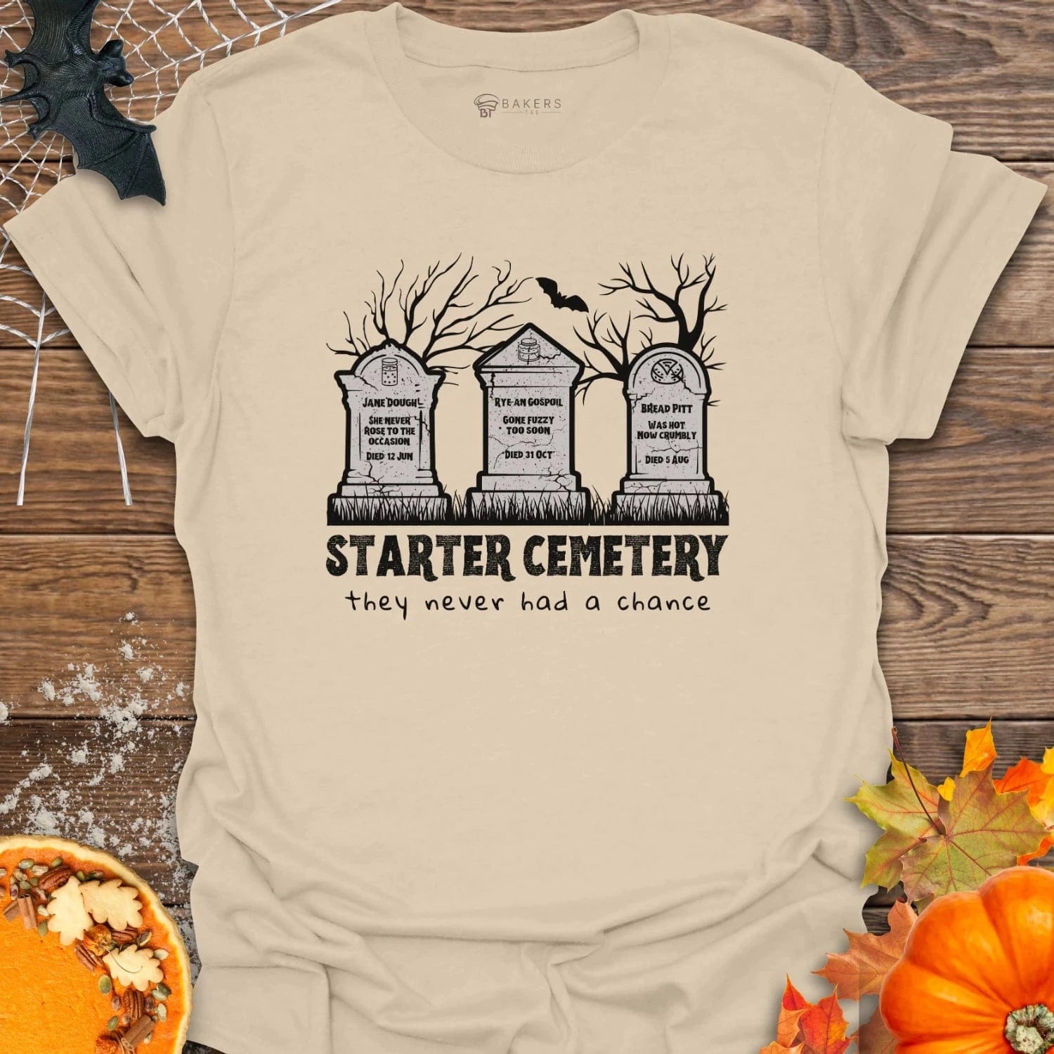 Sand t-shirt with 'Starter Cemetery' graphic design on a wooden surface with Halloween decorations.