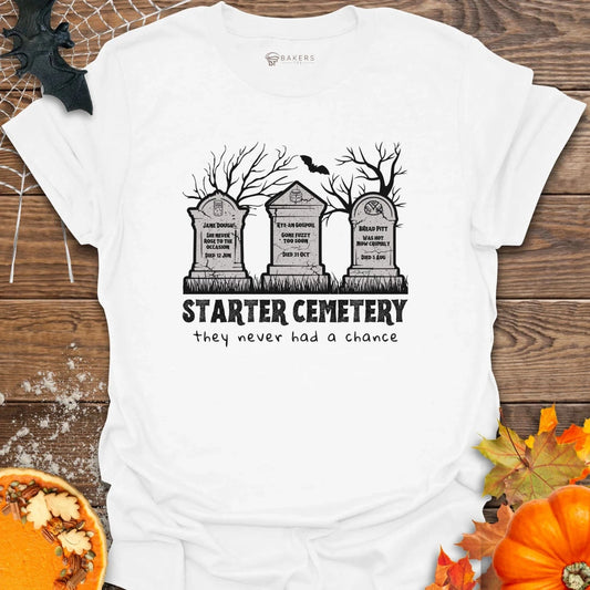 White t-shirt with 'Starter Cemetery' graphic design on a wooden surface with pumpkins and leaves.